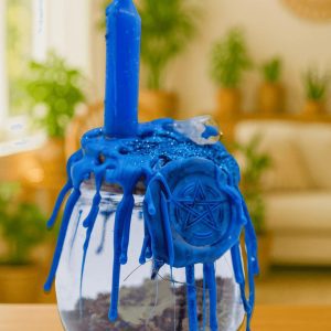 Root Chakra 17 Healing Spell Jar - Large, a glass jar with a blue candle melting over a witch's pentagram charm, with blue wax drippings covering the jar and candle, used for spiritual healing and positive energy.
